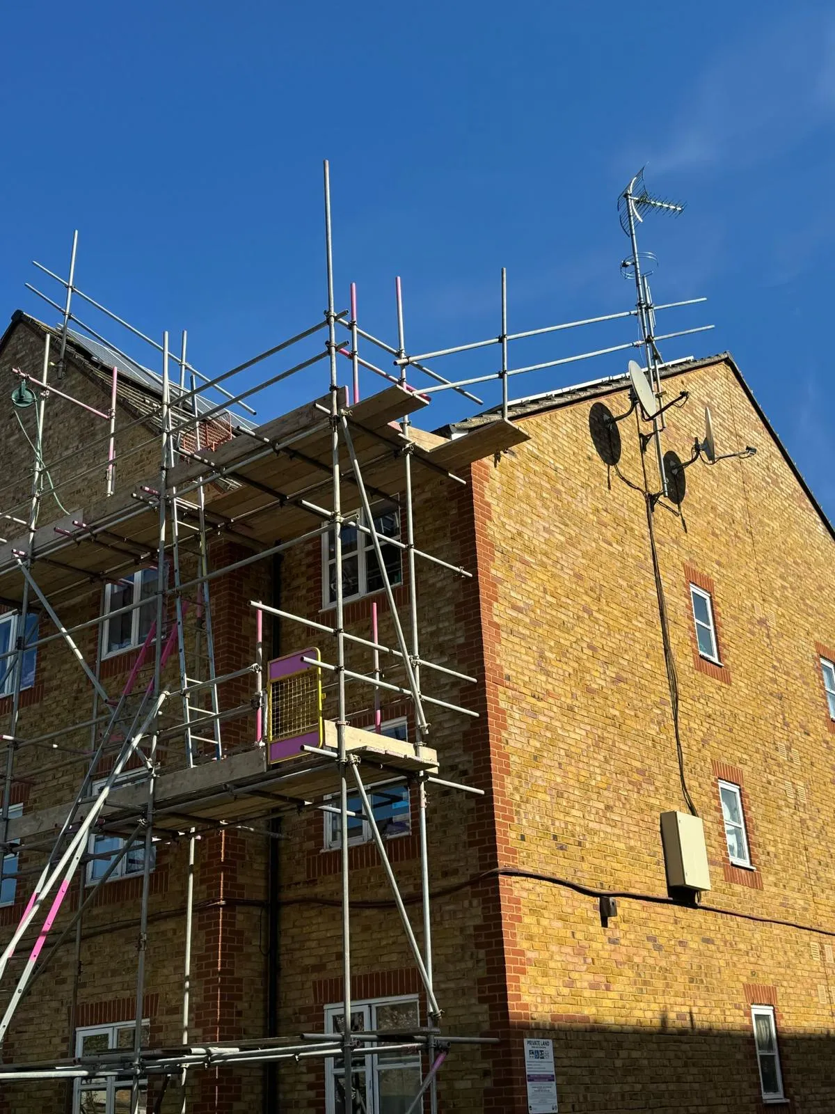 Scaffold platform at roof level on residential block with satellite dishes, Dartford