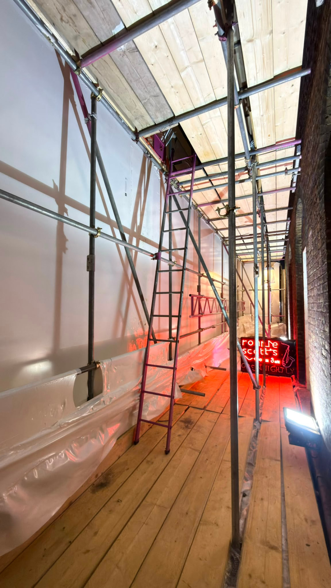 Boarded working lift and ladder access behind the shrink wrap encapsulation at Ronnie Scott's, Soho - Pinnacle Scaffolding