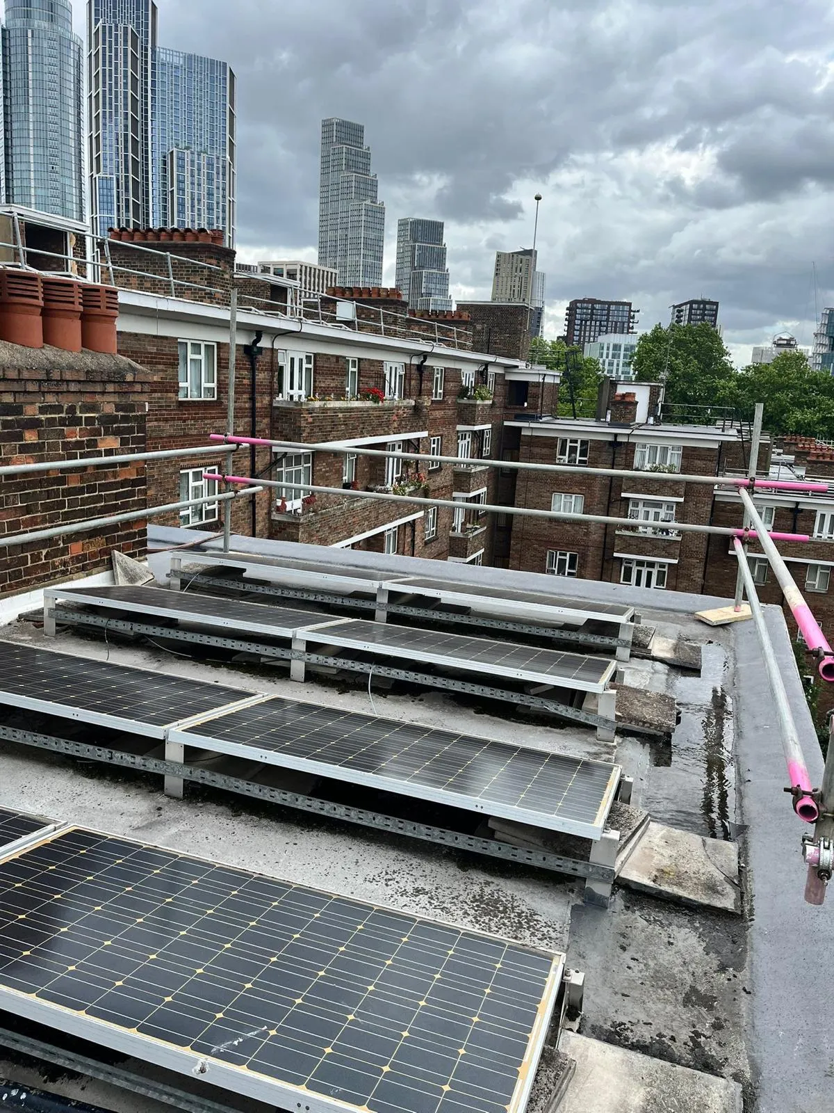 Flat roof solar panel array with scaffold edge protection and London skyline